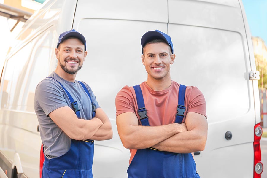 Business Insurance - Two Workers in Blue Overalls and Hats Stand in Front of Their Business's White Van and Smile